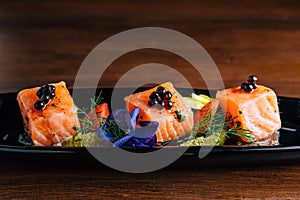 Close up Grilled Medium Rare Salmon Cube topping with caviar and served with strawberry and orange in black plate