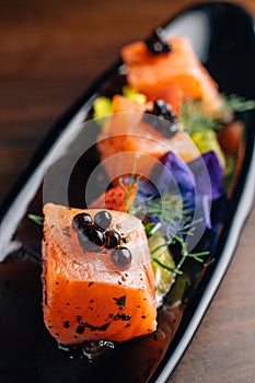Close up Grilled Medium Rare Salmon Cube topping with caviar and served with strawberry and orange in black plate