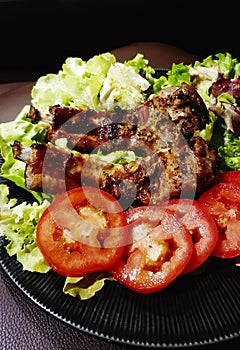 Close up grilled ribs steak with fresh sliced tomato, green cabbage and spinach on black dish or plate.