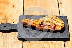 Close up of grilled steak on small black chopping board isolated. Barbecue, grill and food concept