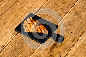 Close up of grilled steak on small black chopping board isolated. Barbecue, grill and food concept