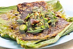 Close-up of grilled stingray fish with spices topped with okra vegetable on banana leaf popular food in Malaysia