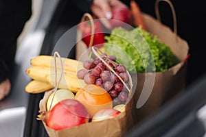 Close-up of groceries in eco package in car trunk. Hands of female packing vegetables and fruits after shipping in