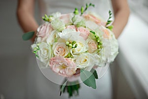 Close-up groom in a suit and the bride in a white dress are standing and holding a bouquet of peach roses, eustomas and