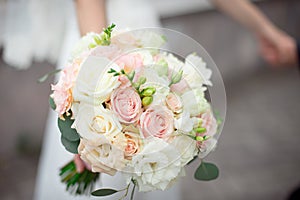 Close-up groom in a suit and the bride in a white dress are standing and holding a bouquet of peach roses, eustomas and