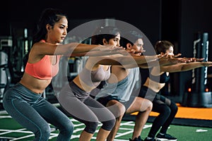 Close-up of Group of athletic young Asian people in sportswear doing squat and exercising at the gym.