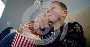 Close up. Group of children watching movie on TV in the evening at home and eat popcorn.