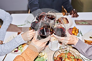 Close up of group of friends toasting with red wine glasses at dinner table