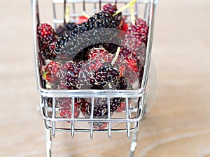 Close up group of mulberries in red shopping cart on wooden table. Mulberry this a fruit and can be eaten in have a red and purple