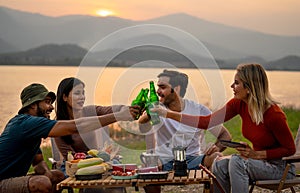 Close up group of multi-ethnic friends men and women sit on chair with party and camping together also cheers with bottle near