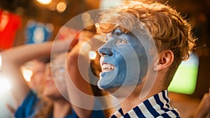 Close Up on a Group of Supportive Soccer Fans with Painted Blue and White Faces Standing in a Bar