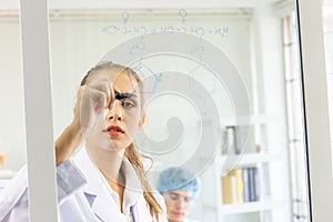 A close-up of a group of young scientists is saving a formula on a glass board