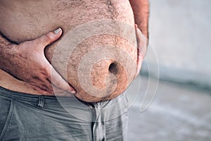 Close-up of a grown man`s round and full hairy belly, with both hands holding it up