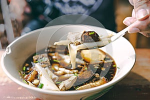 Close up Guay jub, gravy noodle soup  thai street food on wooden table with hand and fork photo