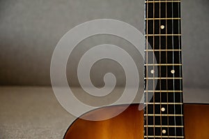 Close-up guitar fretboard with strings isolated on a blurred gray background with copy space. Music concept. Gray fabric surface.