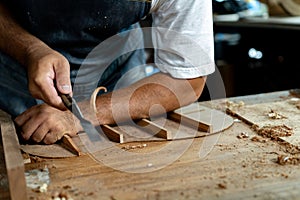 Close-up of guitar luthier using chisel to shave bracing of acoustic guitar