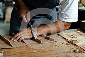 Close-up of guitar luthier using chisel to shave bracing of acoustic guitar