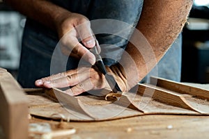 Close-up of guitar luthier using chisel to shave bracing of acoustic guitar