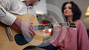 Close-up guitar with male hand playing and blurred woman listening to music at background. Relaxed Caucasian