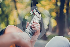 Close up guitar neck with capo in the park. Young man sitting on the bench in the park playing the guitar