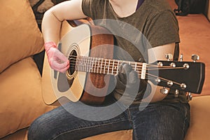 Close-up of a guy playing guitar on the couch at home. Stay at home. Toned. Selective focus on the hand with the pick