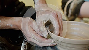 Close-up of guy`s hands making bowl with clay on pottery wheel in workshop