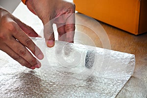 Close up of a guy`s hands using bubble wrap to pack a glass bottle before put into cardboard box deliver to customer