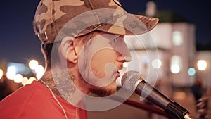 Close-up of a guy singing with a guitar into the microphone. Speech at night in the city square. Beautiful lighting.