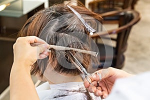 Close-up of hair dresser barber cutting hair of female client with scissors and comb