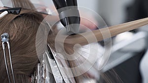 Close up, hairdresser dries woman hair with hairdryer during hair coloring