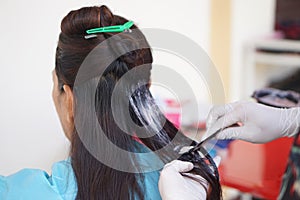 Close up hairdresser hands wears gloves, apply dye color cream on client's hair.