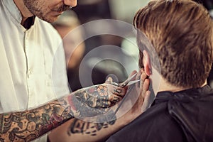 Close up hairdresser with scissors cut the beard