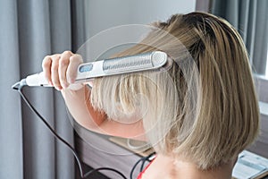 Close-up of a hairdresser straightening gold hair with hair iron
