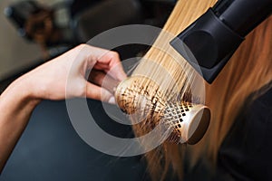 Close-up of hairdressers hand drying blond hair with hair dryer and round brush. Doing hairstyle in beauty salon