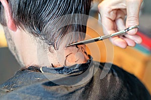 Close up of hairstylist`s hands cutting strand of man`s hair. Professional hairdresser or barber occupation.