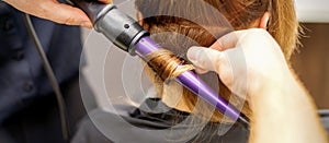 Close up of hairstylist's hands using a curling iron for hair curls in a beauty salon.