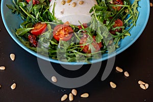 Close up of a half blue plate of cheese salad with cherry tomatoes, arugula and pinions
