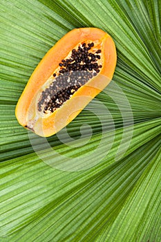 Close up on the half cut of fresh ripe papaya on green palm leaf.