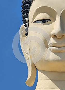 Close-up of the half-face of the pale yellow stone Buddha image at the outdoor courtyard of Wat Kingkaew. Thailand-Buddhism