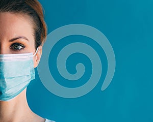 Close-up half face of young woman in medical mask on blue background.