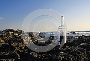 Close up of  half full red wine bottle and single glass on rocks of beach with ocean waves background - El Cotillo,