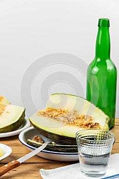 Close up of half green melon with knife on wooden table with green bottle