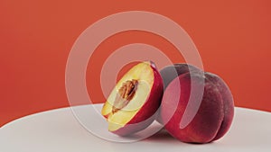 Close up half of nectarine, two peaches on rotating table on orange background
