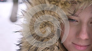Close-up half-portrait of beautiful young caucasian girl in fur hood prettily smiling into camera on winter street