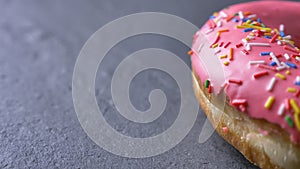 Close-up half-shot of delicious pink donut with multicolored chips and eyes spinning slowly on gray table background.