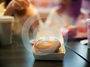 Close-up of hamburgers in a box. Two best friends talking in a fast food restaurant with burgers, fries and drinks on the table