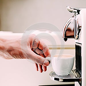 Close up of hand of barista brewing coffee using a coffee machine. The man is standing and holding a white cup