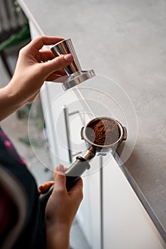Close-up of hand of barista tamping coffee in portafilter before making coffee in machine