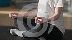 Close-up hand of blurred pregnant woman sitting in lotus pose on exercise mat training indoors. Unrecognizable young