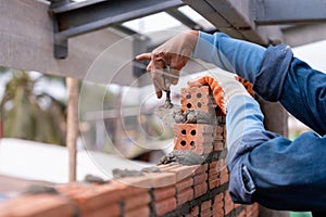 Close up hand of Bricklayer worker installing brick masonry on exterior wall with trowel putty knife on construction site